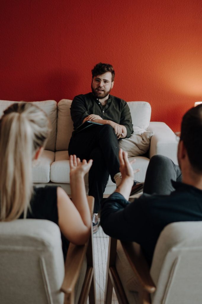 Therapiegespräch in einem Raum mit roter Wand und heller Couch